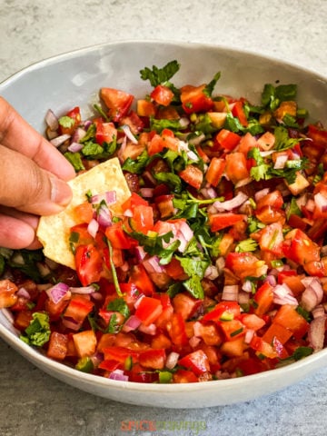Hand dipping in bowl of pico de gallo with tortilla chip