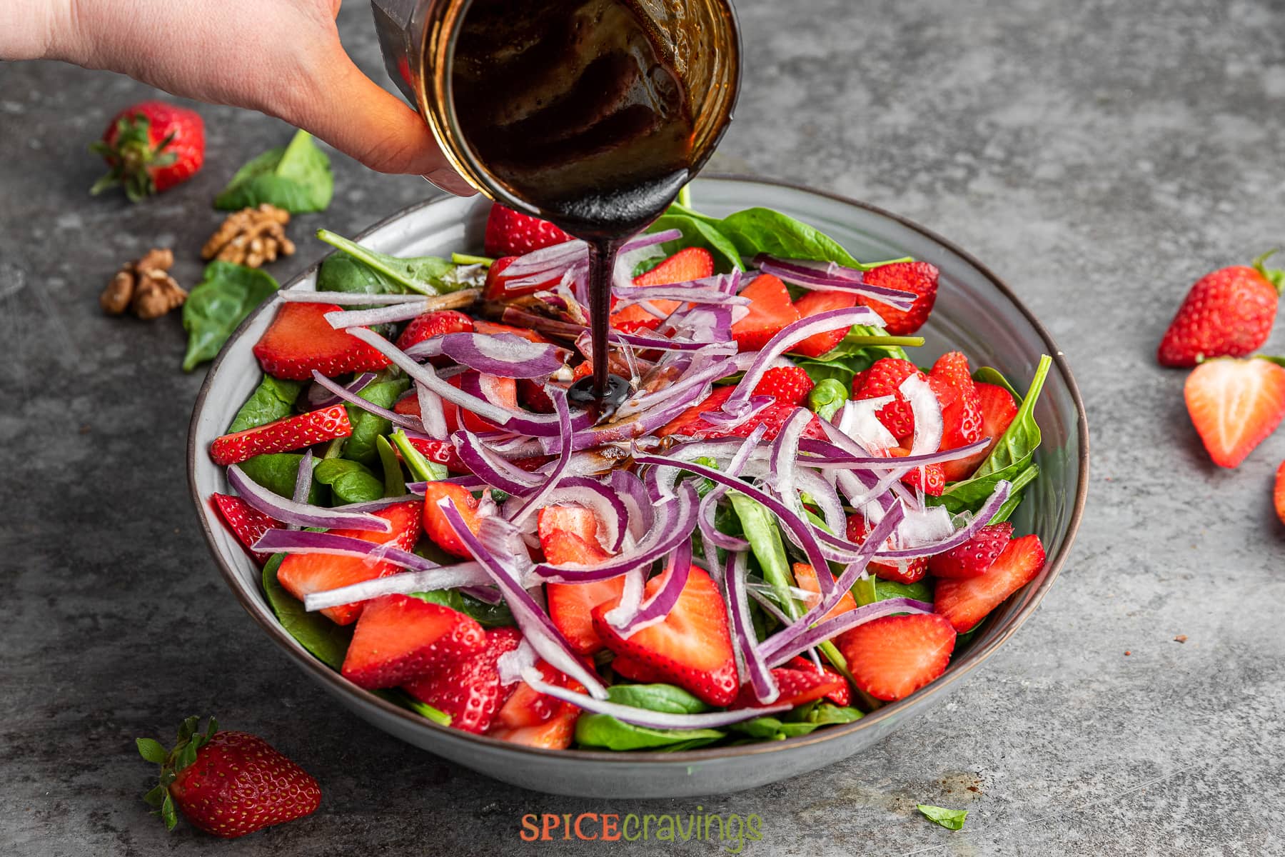 pouring honey balsamic vinaigretta over strawberry and spinach salad in bowl
