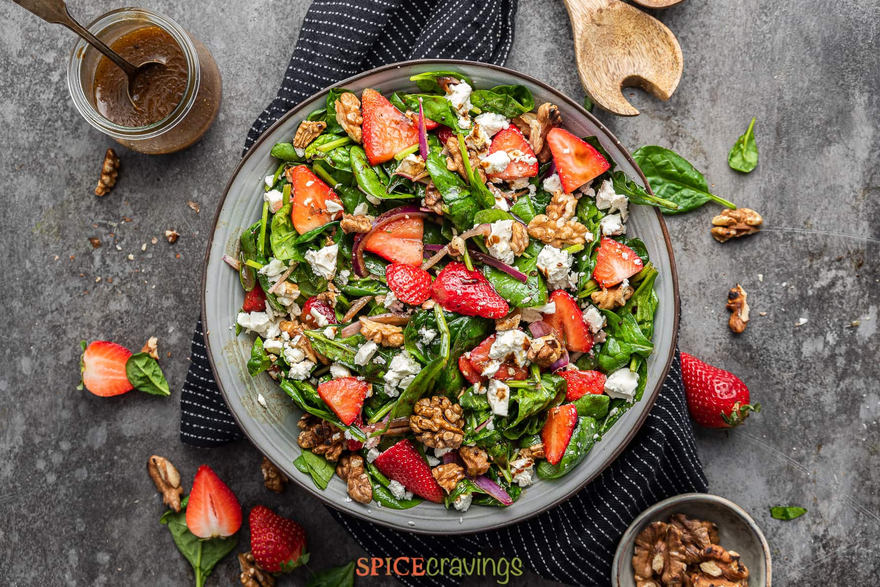strawberry spinach salad in large bowl with honey balsamic dressing and walnuts on the side