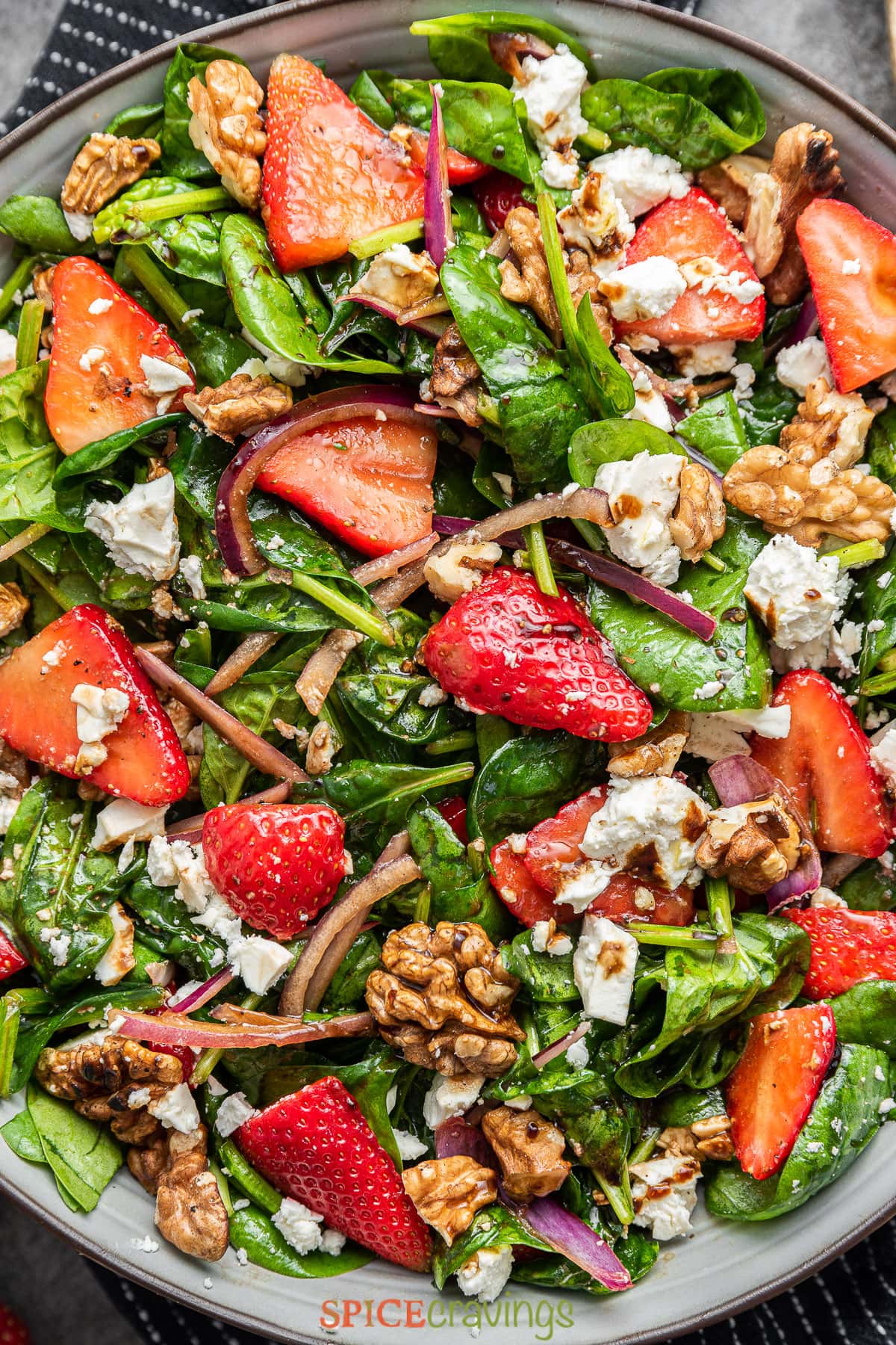 strawberry spinach salad recipe topped with feta cheese and nuts in large bowl