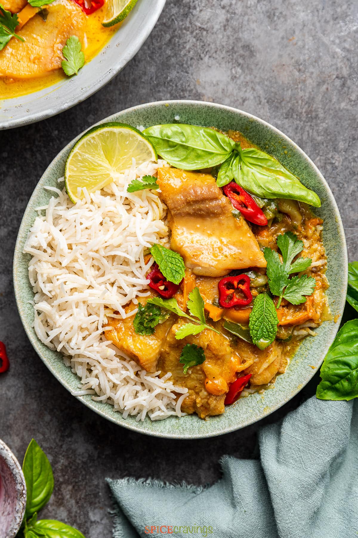 Yellow fish curry with rice in a bowl garnished with fresh herbs