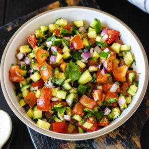 chopped salad made of cucumber, tomato and onion in white bowl