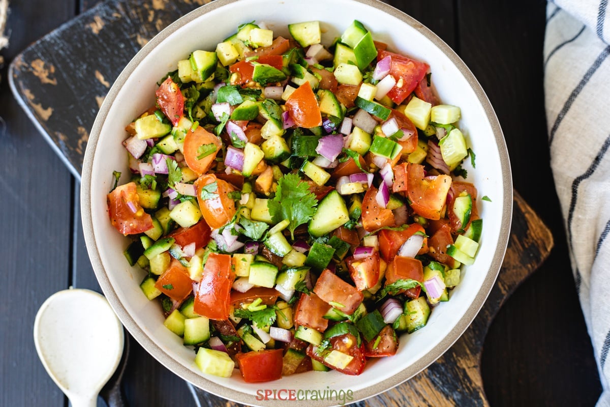 chopped salad made of cucumber, tomato, cilantro, and onion in white bowl