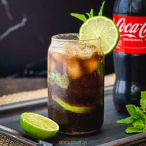 Glass of coke with lime and mint next to a bottle of coke