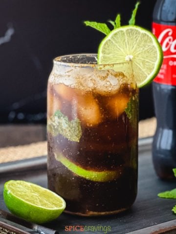 Glass of coke with lime and mint next to a bottle of coke