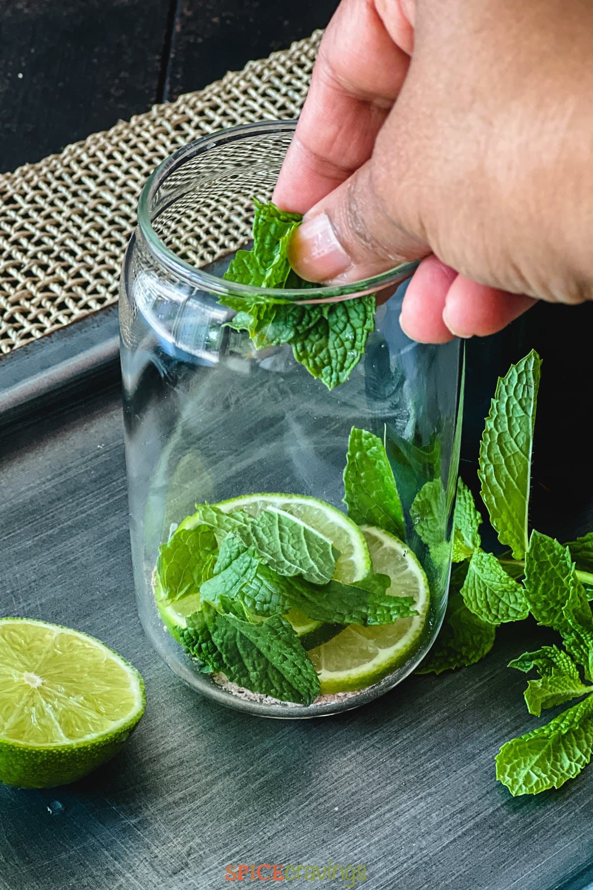 Hand adding mint leaves to glass with lime slices and spices