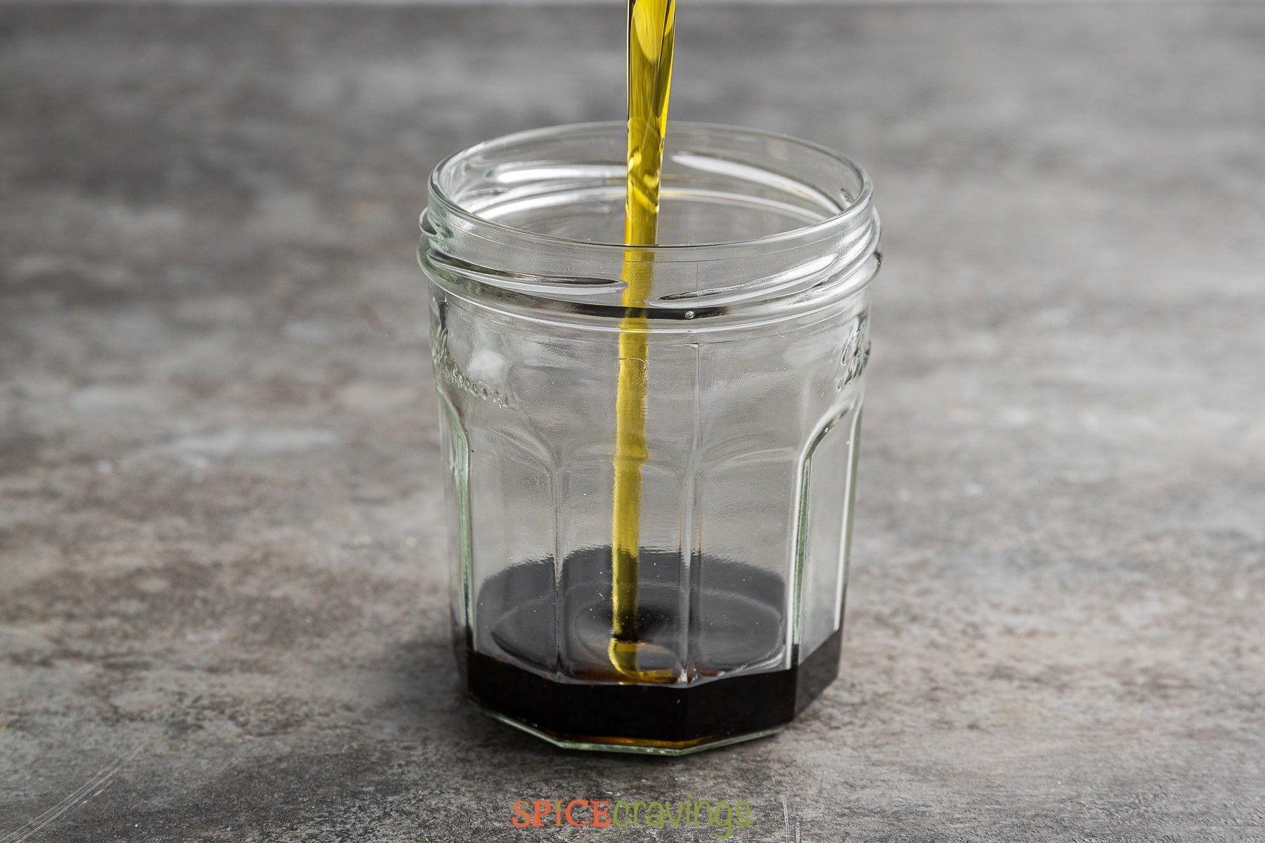 olive oil pouring into glass jar with balsamic vinegar