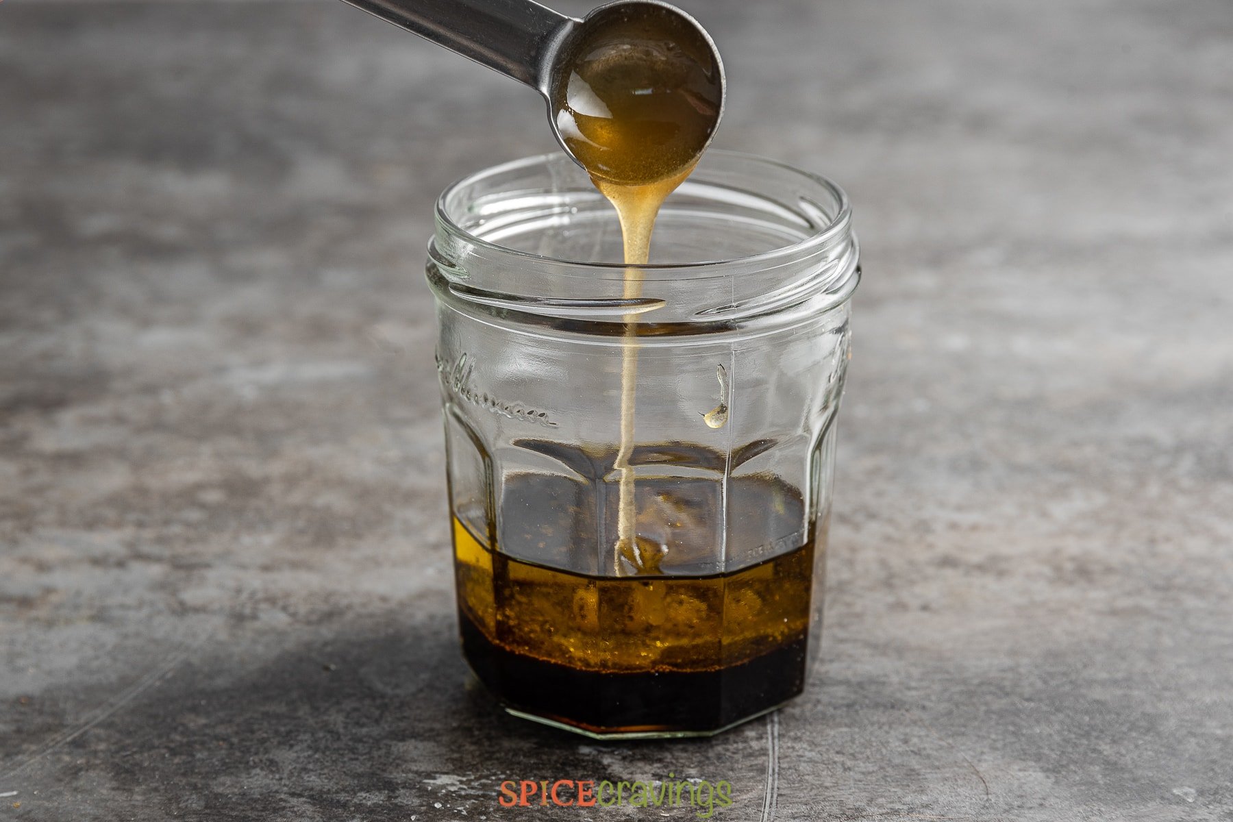 pouring honey into glass jar with balsamic vinegar and olive oil