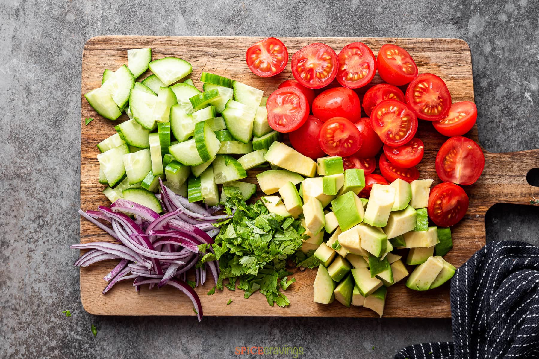 Chopped cucumber, tomato, avocado and more on wooden cutting board
