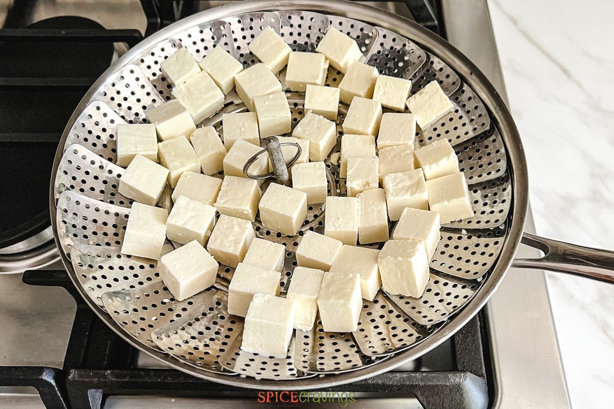 paneer cubes in steamer basket over skillet on stove
