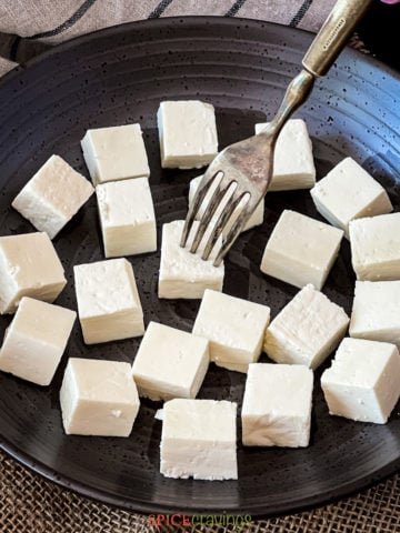 fork digging into paneer cube on black plate