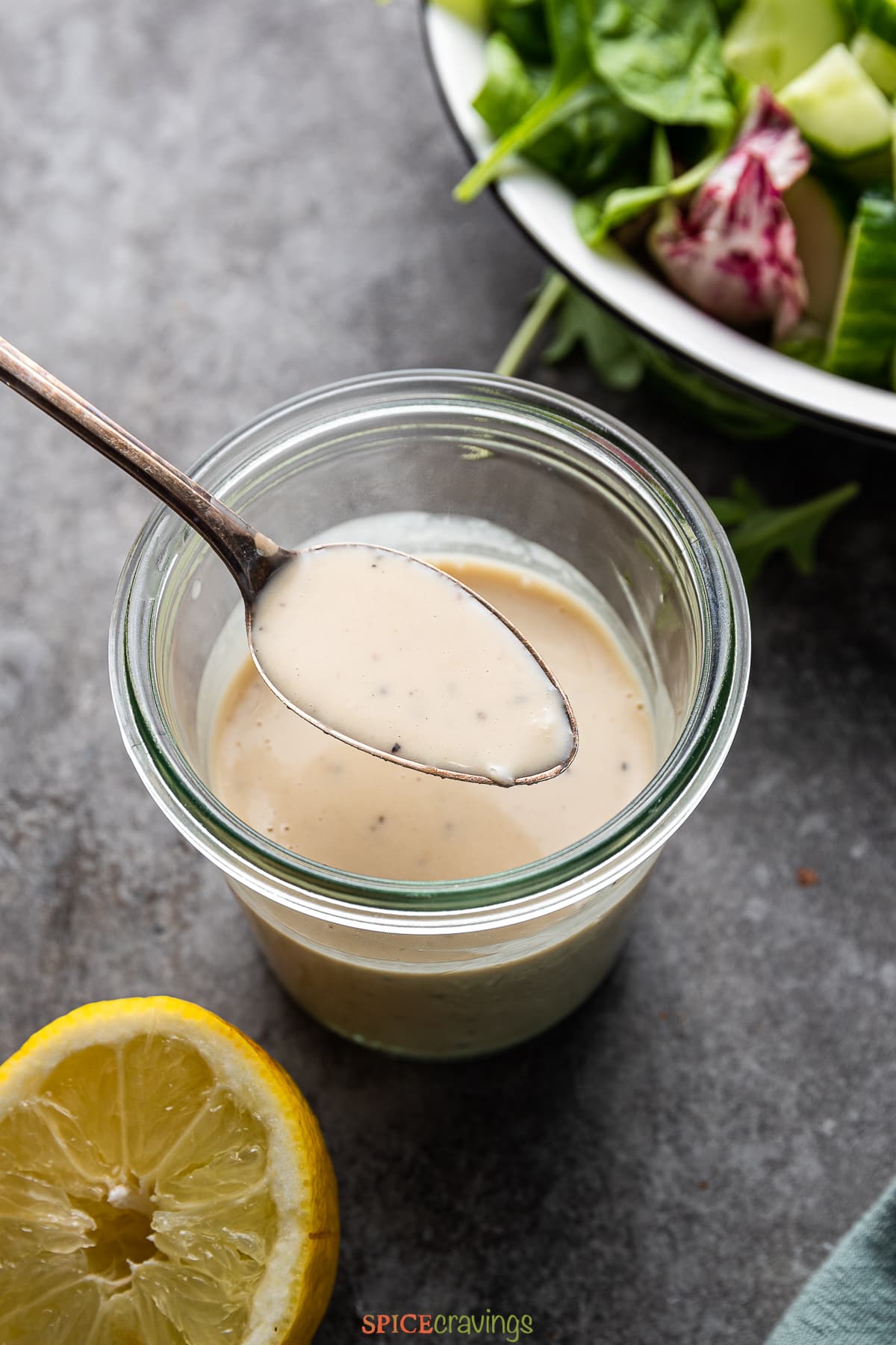 spoonful of creamy tahini dressing over glass jar filled with dressing