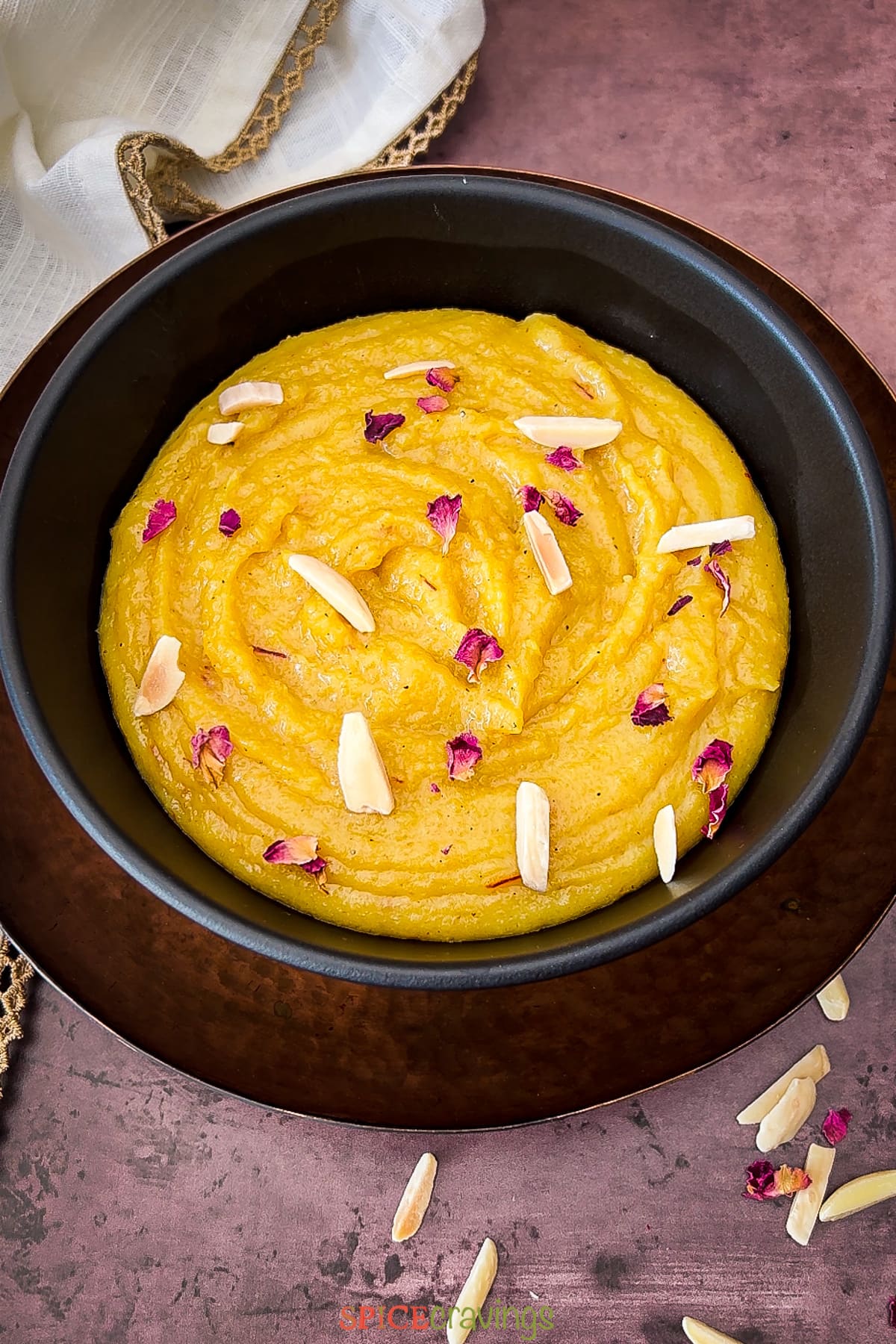 Almond pudding in black bowl garnished with dried rose petals and slivered almonds