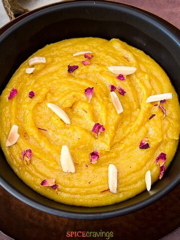 Almond pudding in black bowl garnished with dried rose petals and slivered almonds