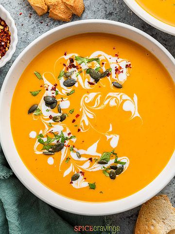 bowl of curry butternut squash soup garnished with pumpkin seeds, cream and herbs
