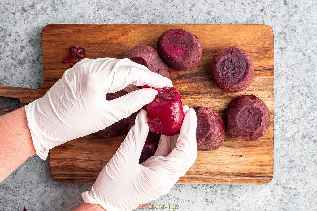 two hands peeling red beets with gloves on
