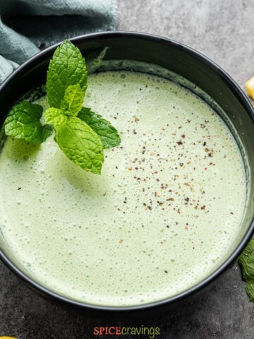 Indian mint yogurt sauce in black bowl with mint sprig