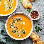 two bowls of curried butternut squash soup garnished with seeds, herbs and coconut milk