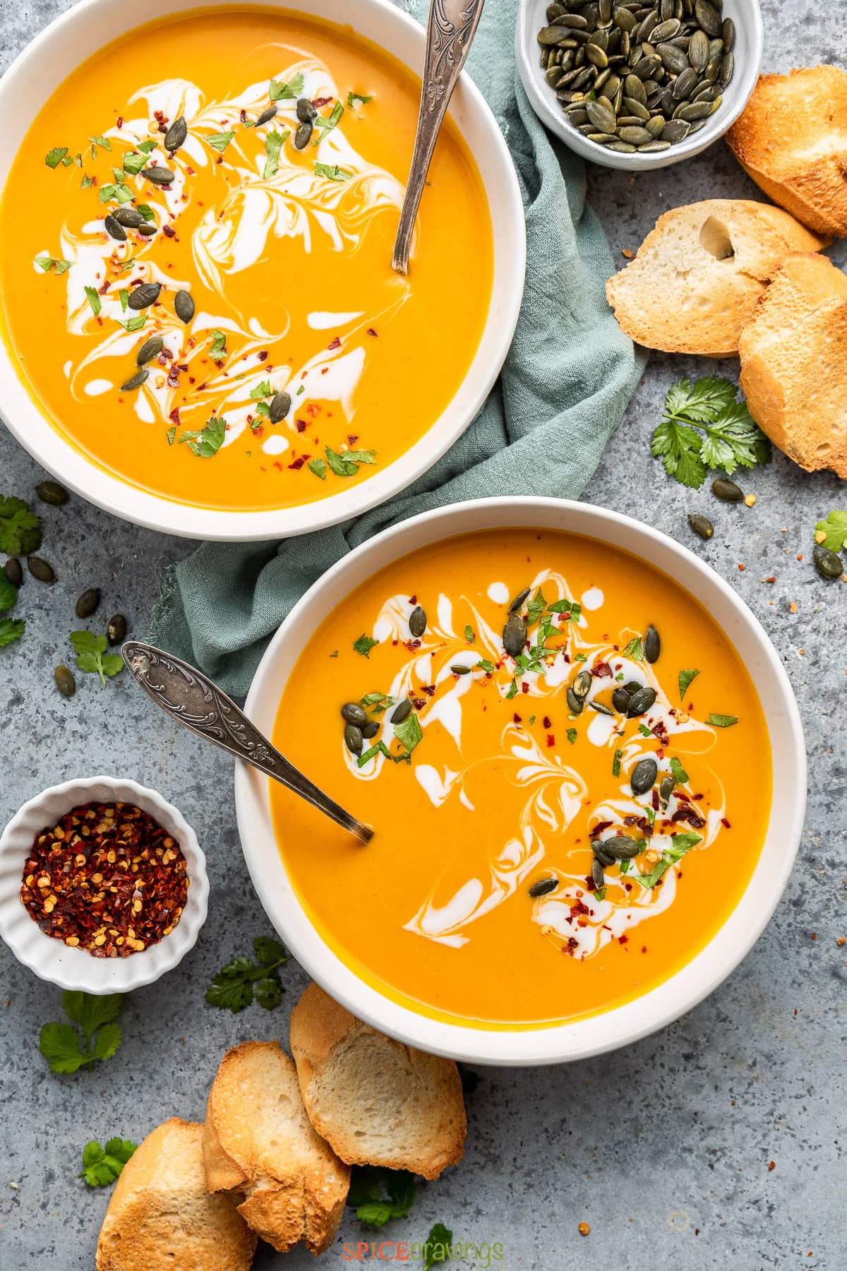 two bowls of curried butternut squash soup garnished with seeds, herbs and coconut milk
