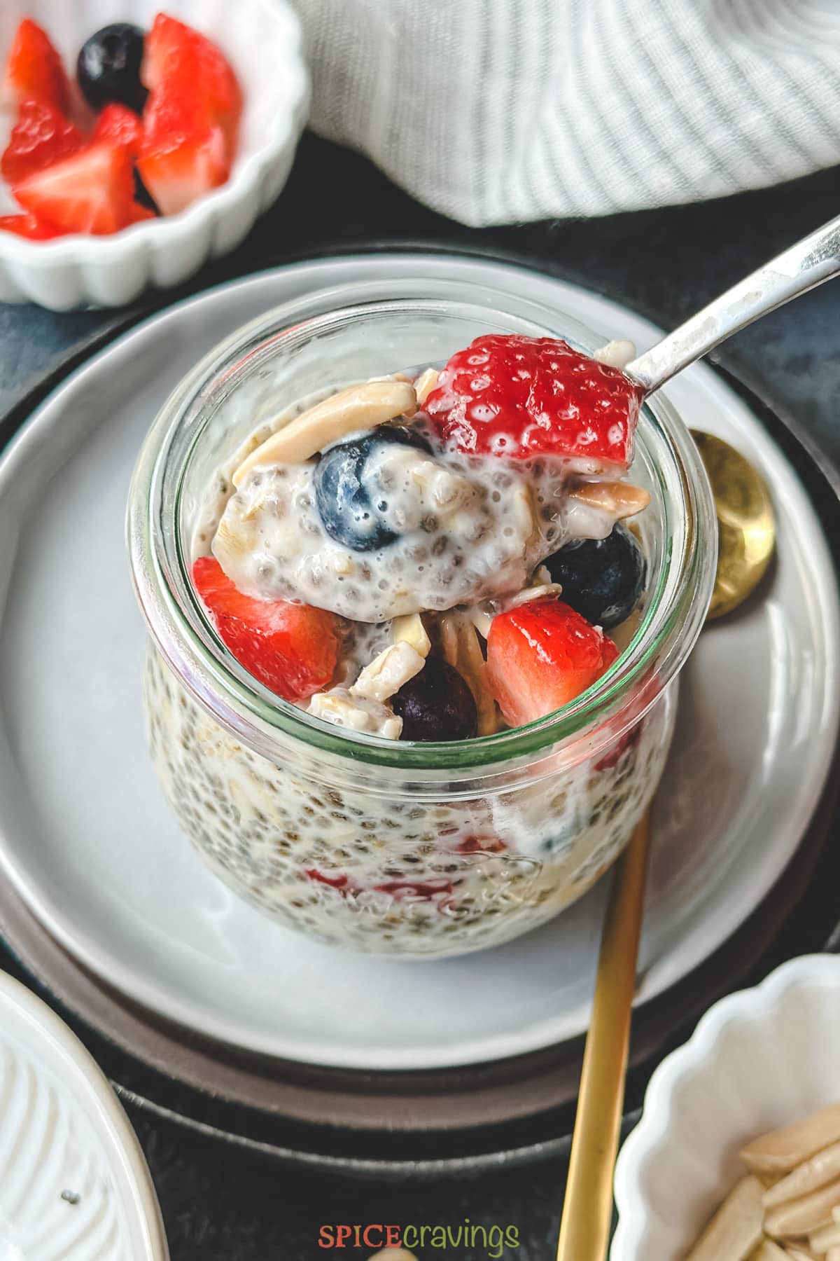 spoon scooping chia seed overnight oats in glass jar topped with berries and nuts