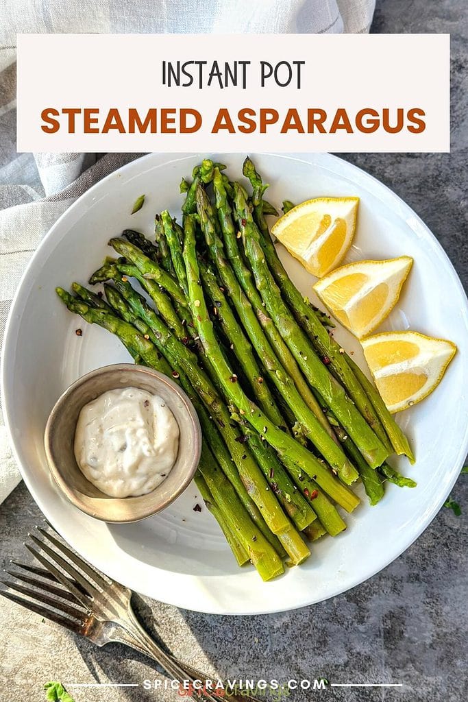 steamed asparagus spears with lemon wedges and dipping sauce on white plate