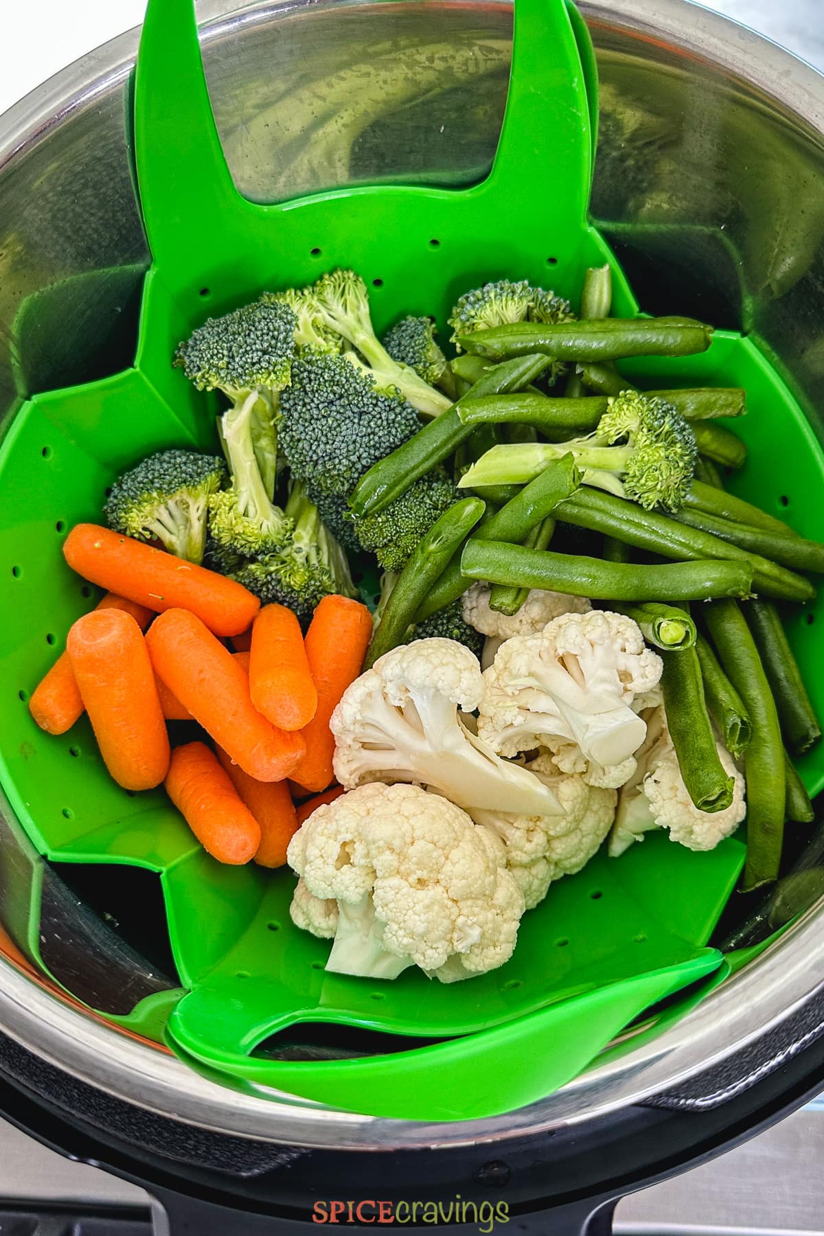 baby carrots, broccoli, cauliflower, string beans in green silicon steamer basket