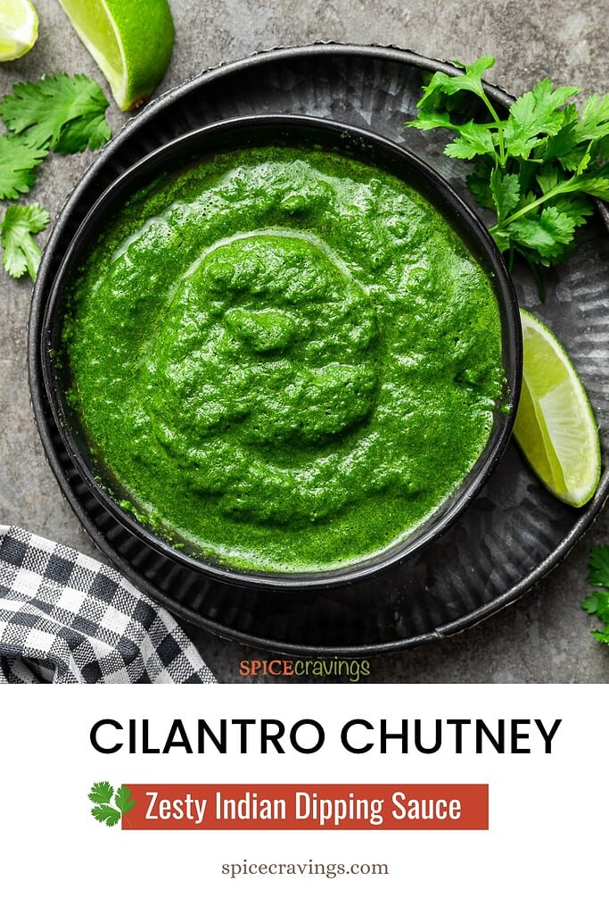 big bowl full of cilantro chutney on metal plate next to cilantro sprigs and lime wedges