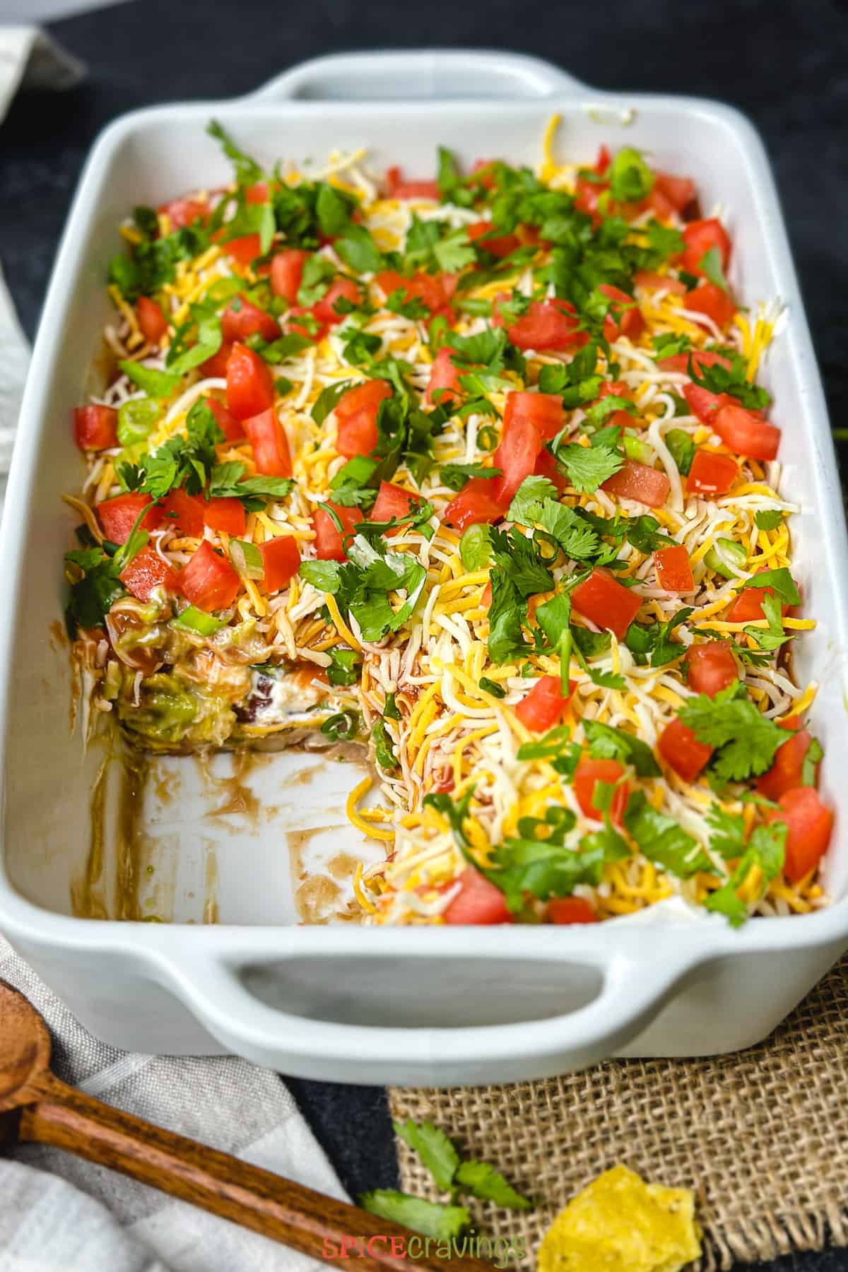 Layered dip in pan showing layers of the dip including beans, guacamole, sour cream and tomato