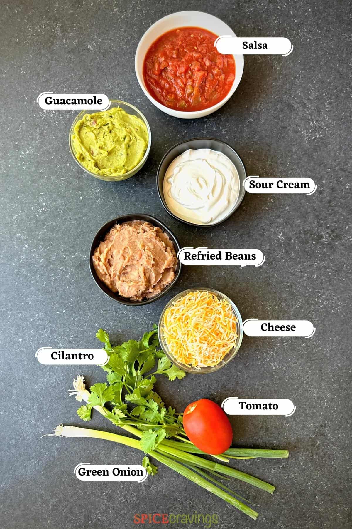 Beans, guacamole, sour cream among other ingredients on grey board