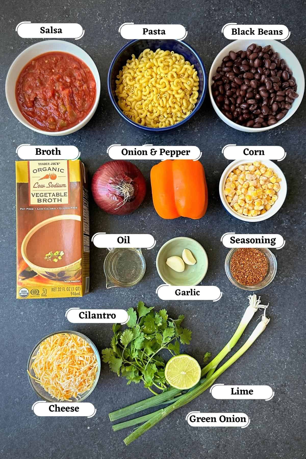 salsa, pasta, beans, spices, and broth, among other ingredients for taco pasta spread out on grey board