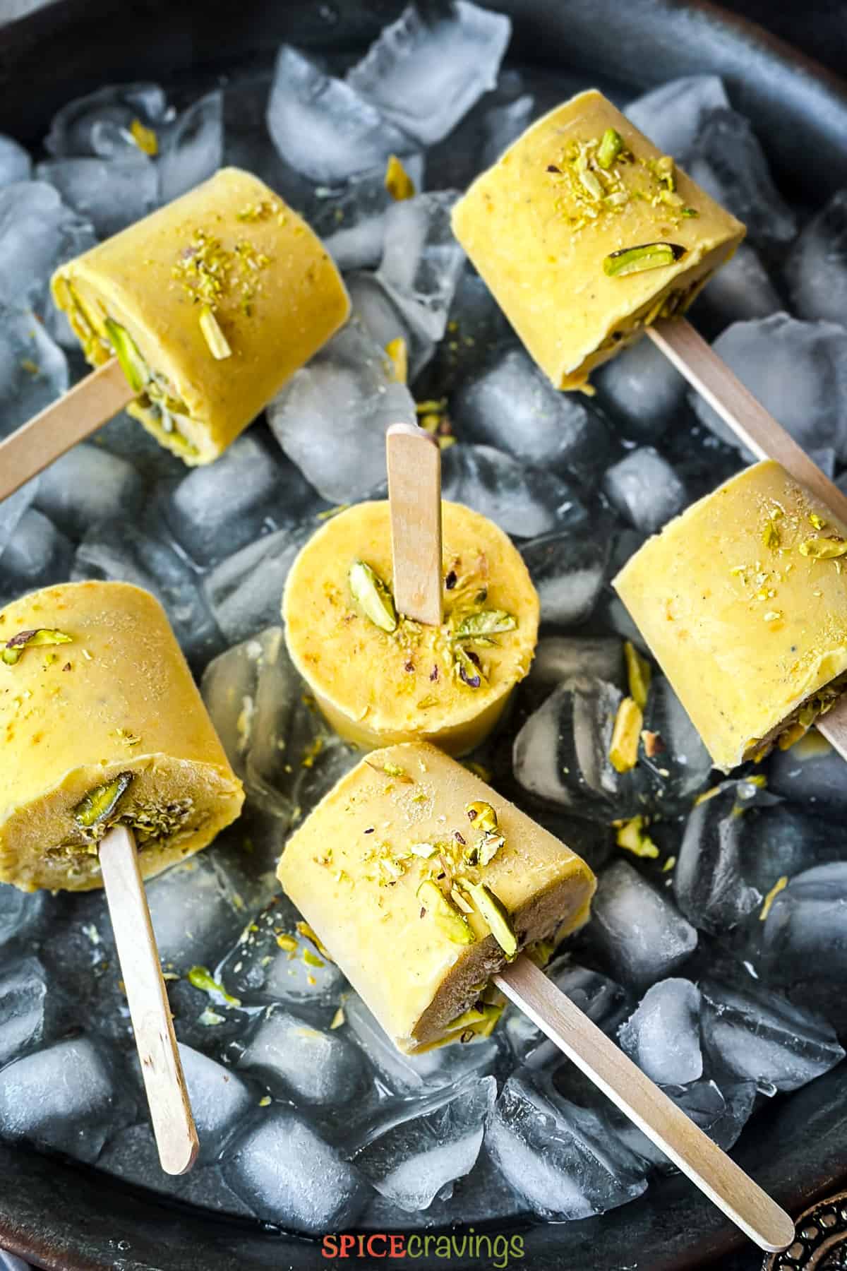 Mango ice cream sticks on a plate of ice cubes garnished with sliced pistachios