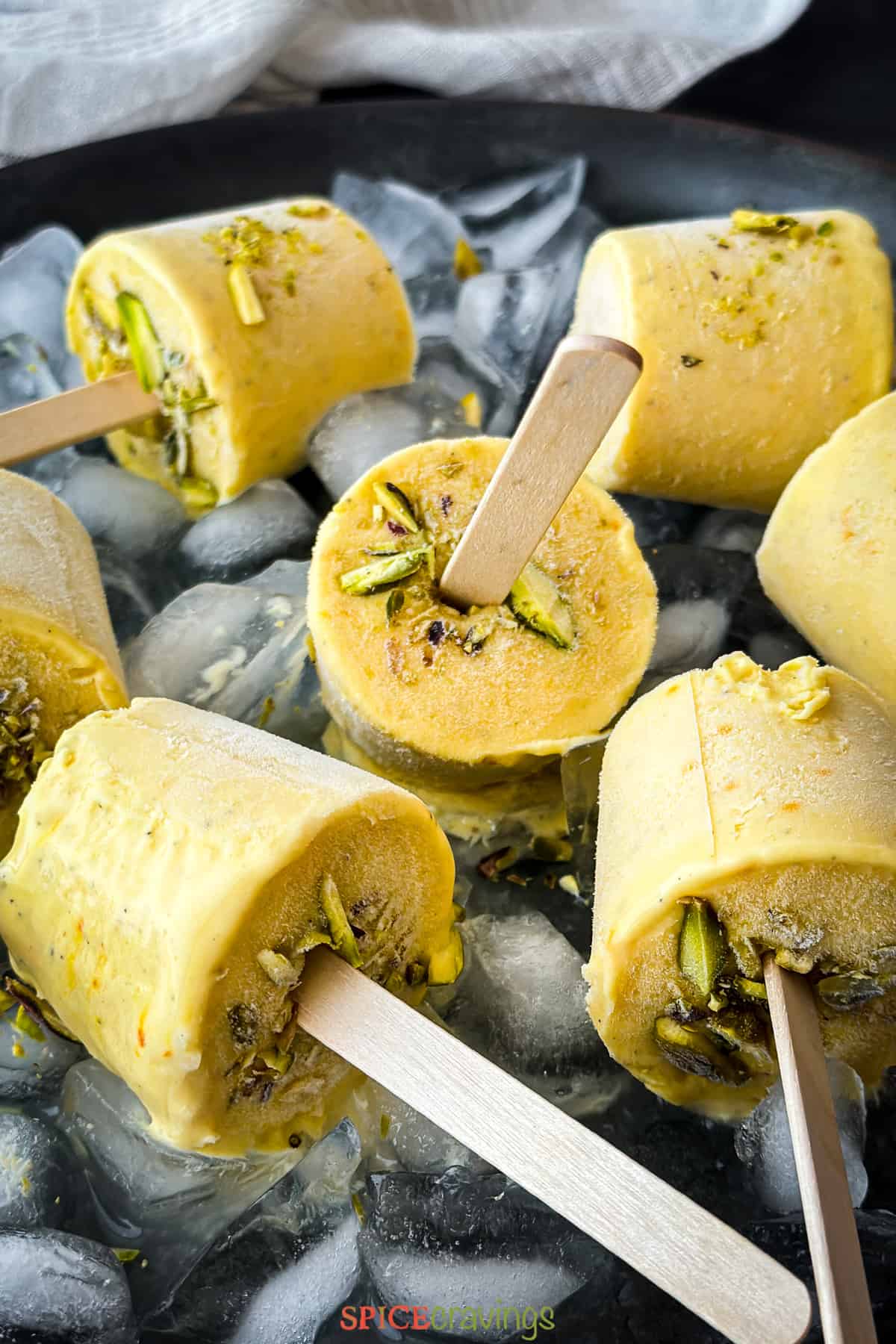 7 Mango ice cream sticks on a plate of ice cubes garnished with sliced pistachio