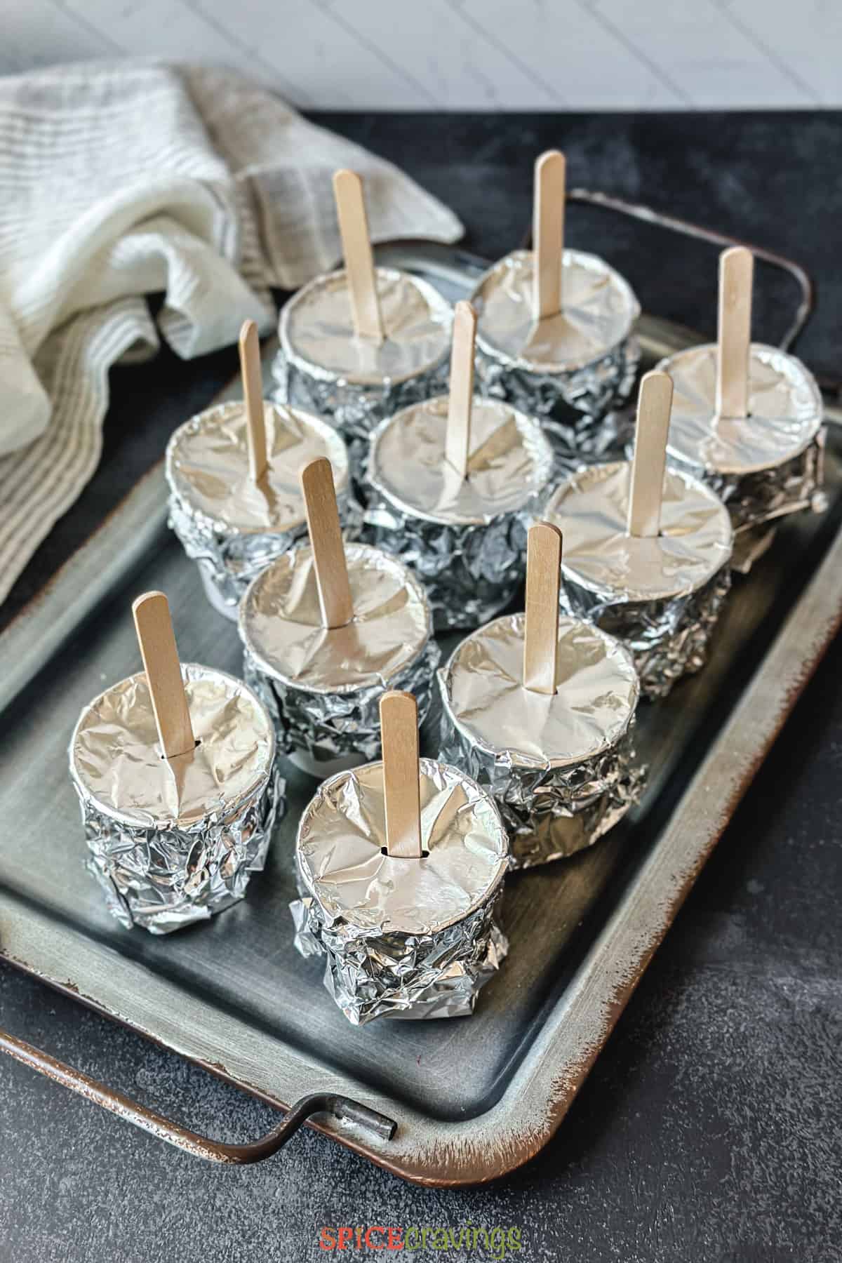 Small cups covered with aluminum foil with ice cream sticks in the middle.
