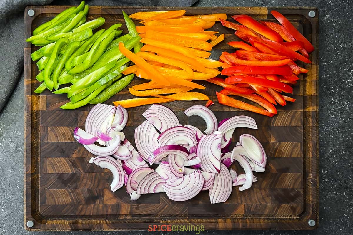 sliced peppers and red onion on wood cutting board