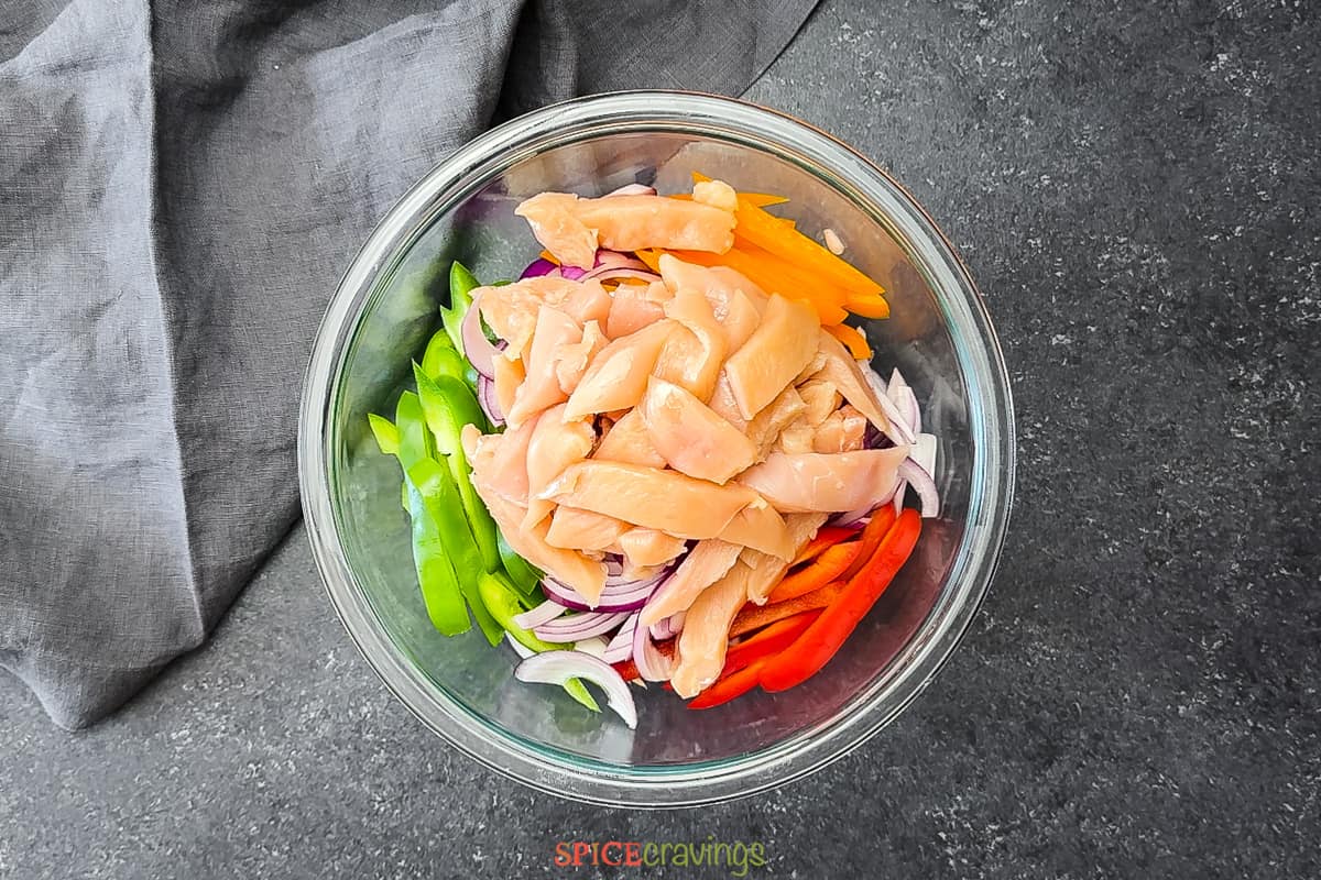 raw chicken strips, sliced peppers and onions in glass bowl