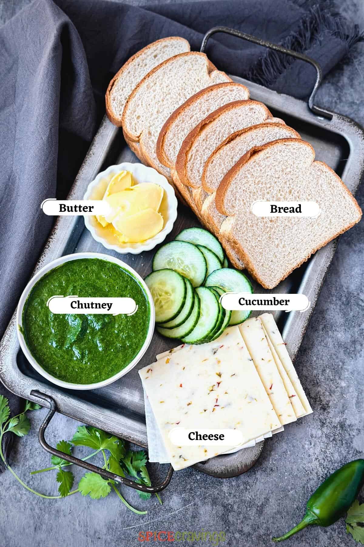 Bread, cucumber and chutney among other ingredients for chutney sandwiches on metal tray