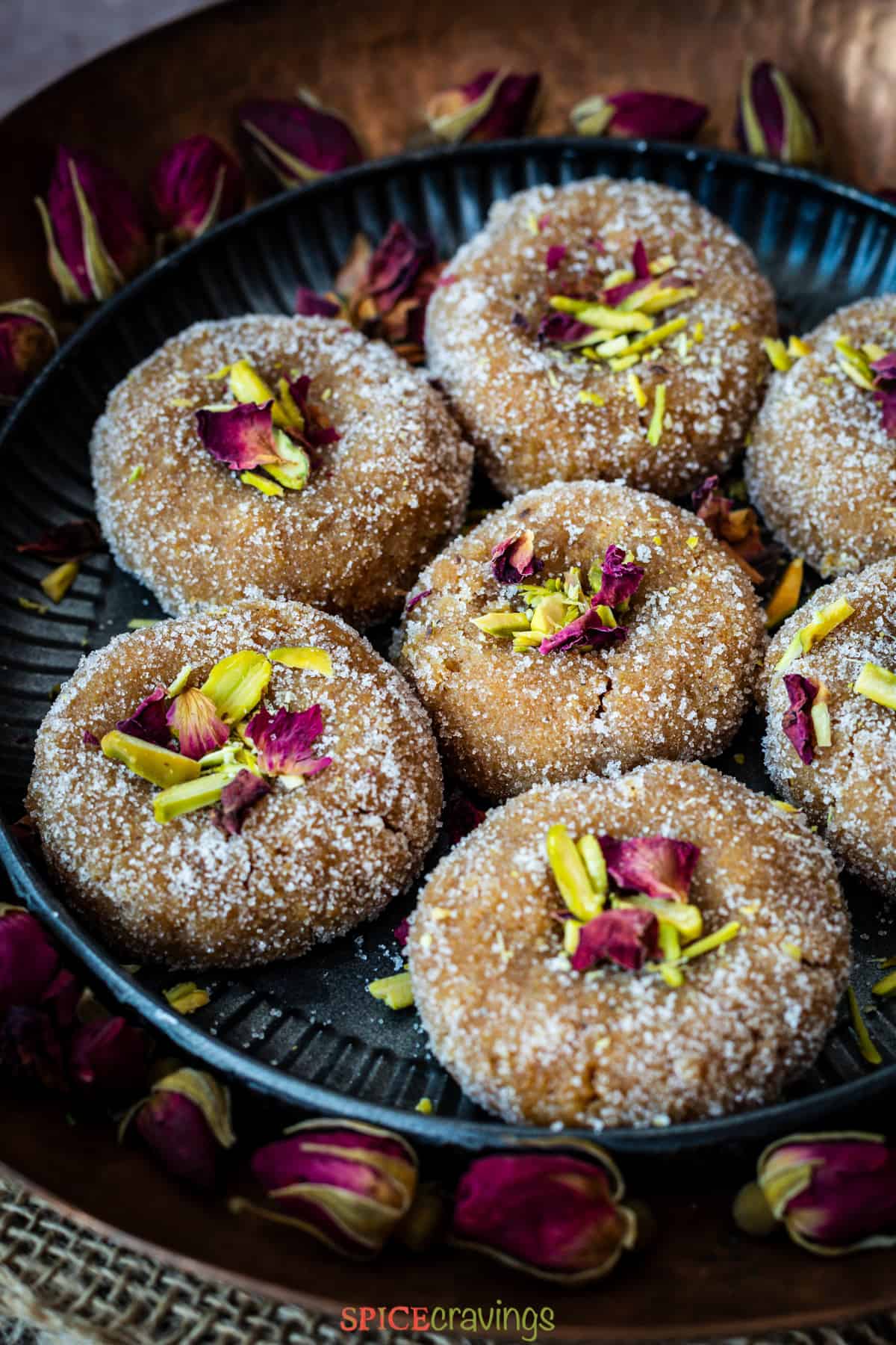 Indian milk fudge called 'peda' on metal plate topped with pistachio slices and rose petals