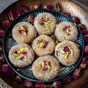 Indian milk-based sweet called mathura peda on metal plate garnished with pistachios and rose.