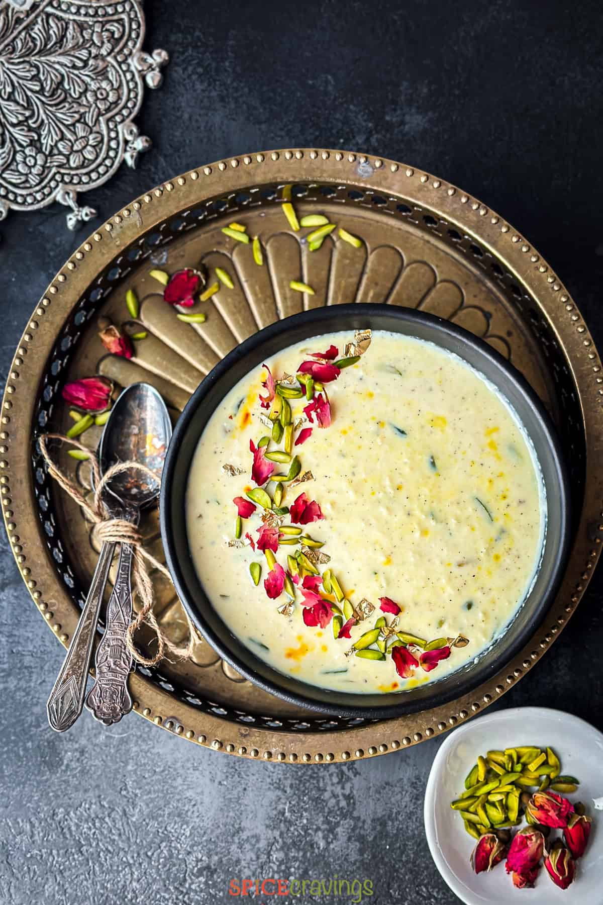 top shot of rabdi, indian dessert, on brass plate garnished with rose and nuts