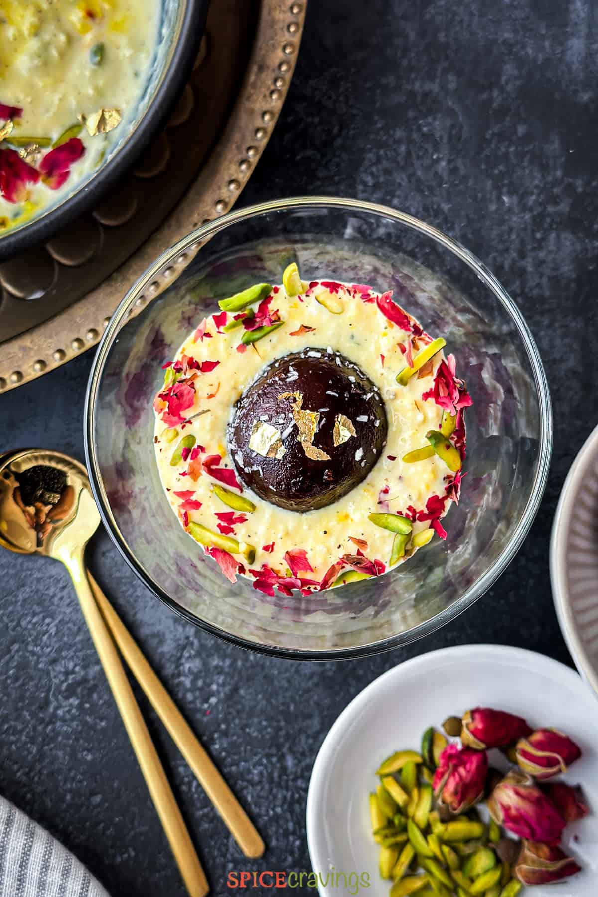 Gulab jamun dipped in a glass of rabdi and garnished with rose and pistachios