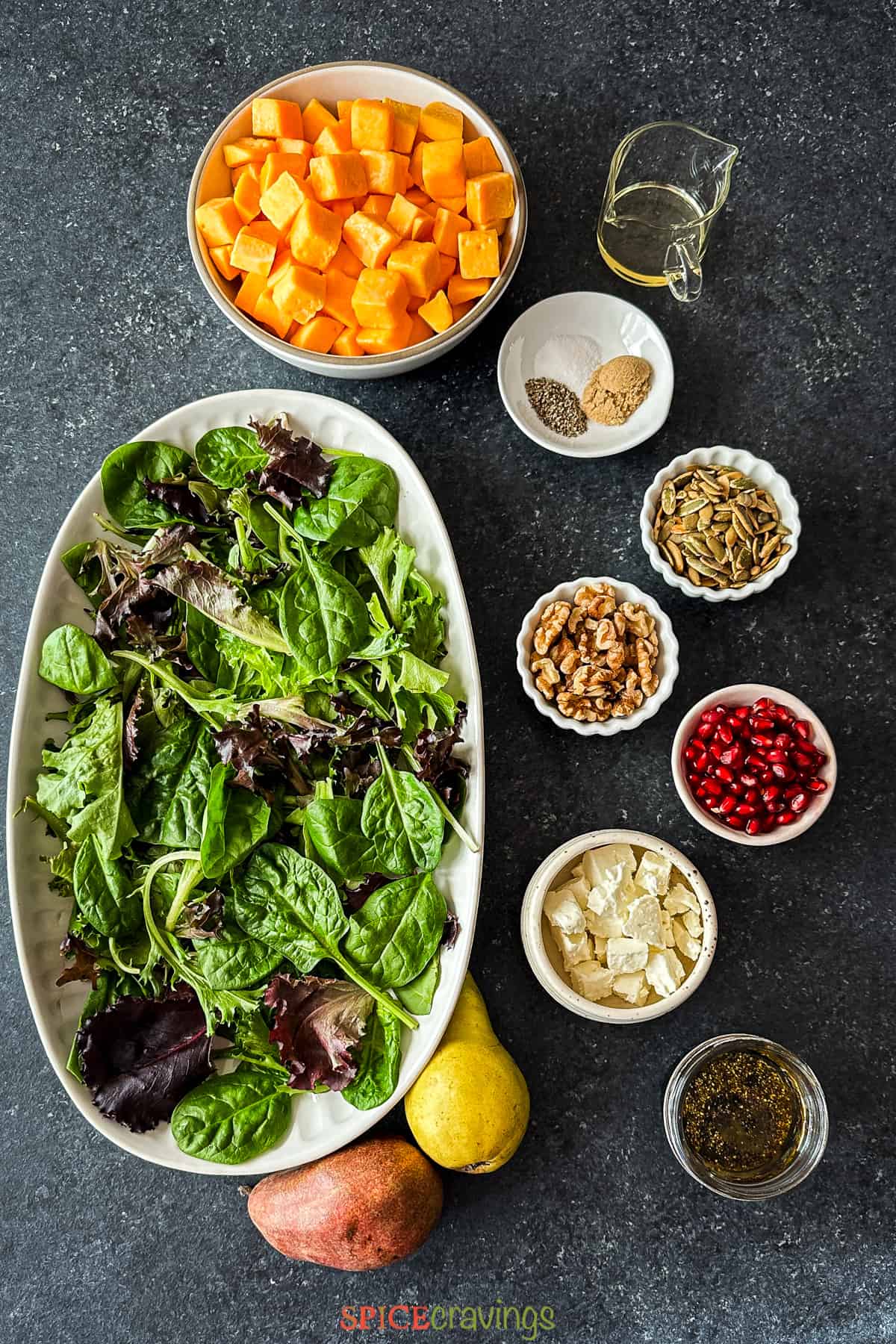 Salad greens, butternut squash, nuts, cheese and other ingredients on a grey board
