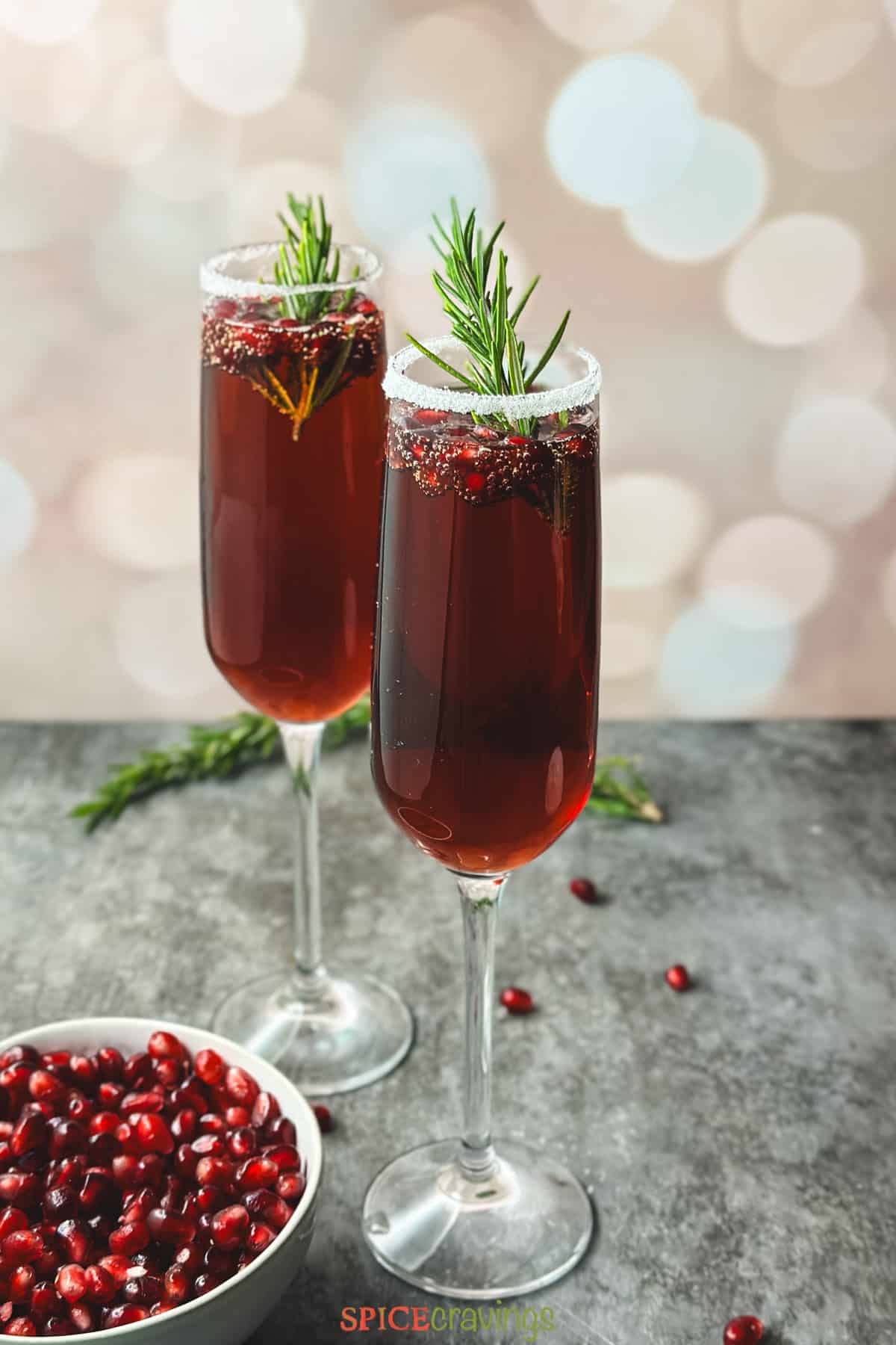 Two glasses of pomegranate mimosa garnished with fresh fruit and rosemary