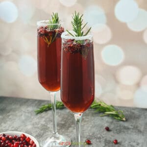 Two flutes with sugar rims and pomegranate mimosa garnished rosemary