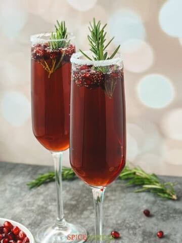 Two flutes with sugar rims and pomegranate mimosa garnished rosemary