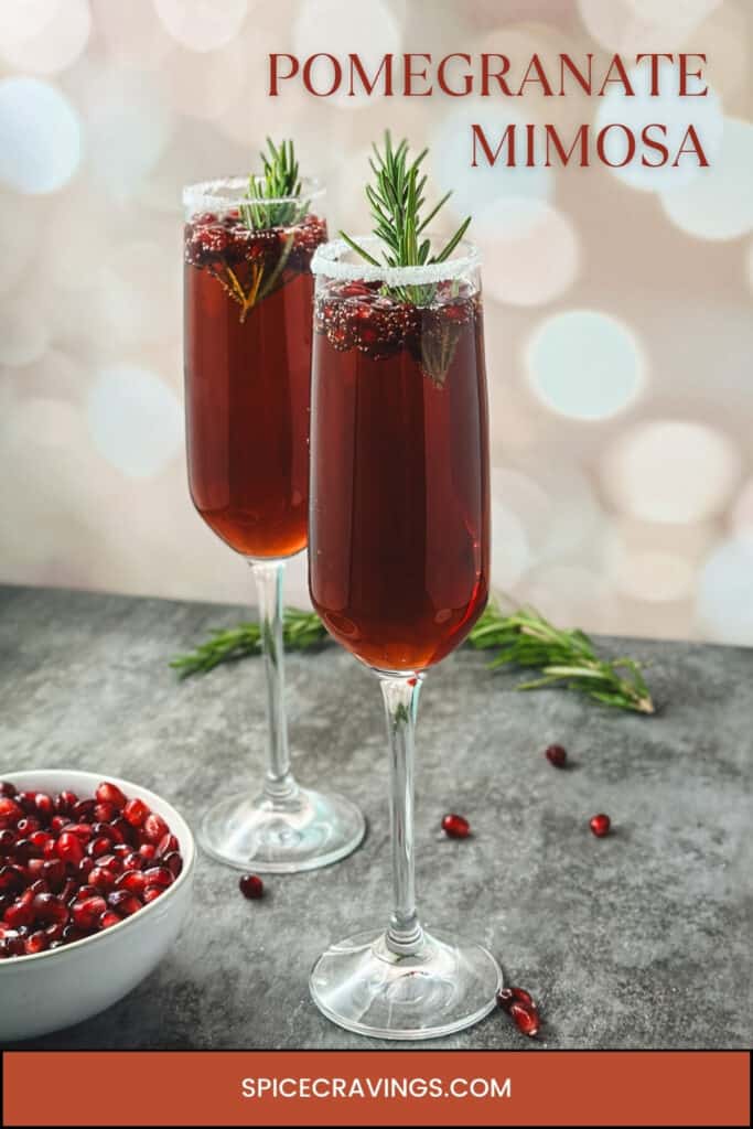 Two champagne flutes with pomegranate mimosa garnished with fresh fruit and rosemary