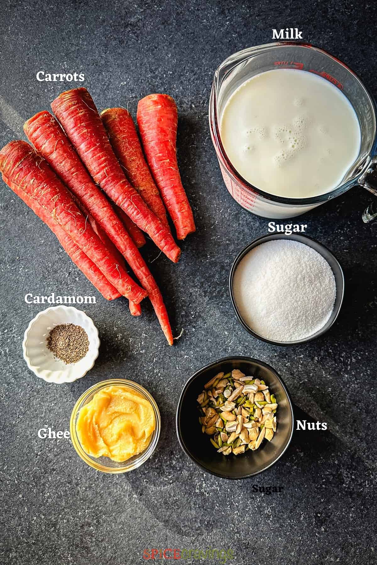 carrots, milk, sugar, ghee, nuts and cardamom on grey board