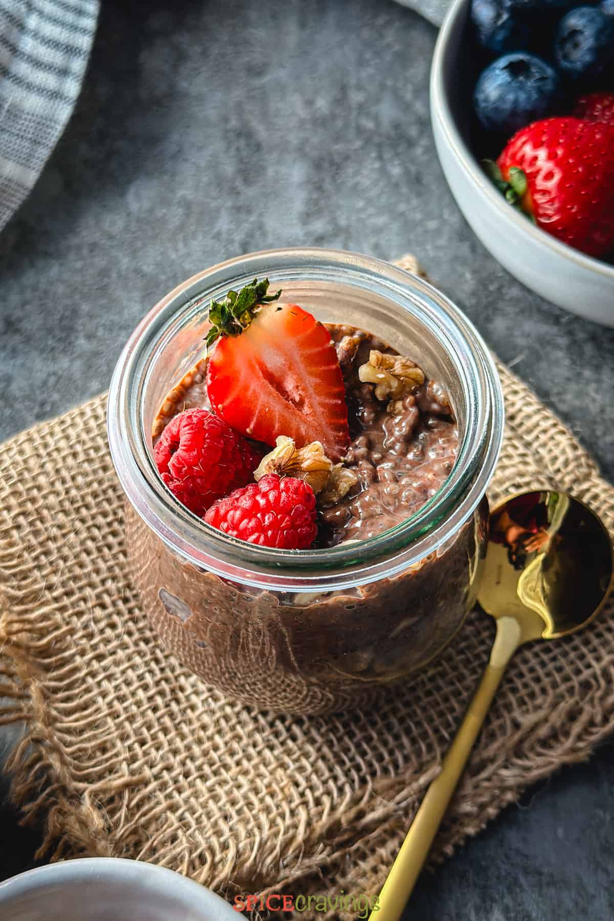 chia chocolate pudding in glass jar topped with strawberry, raspberries, and walnuts