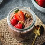 chocolate chia pudding in glass jar topped with strawberry, raspberries, and walnuts