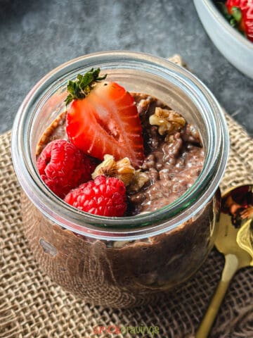 chocolate chia pudding in glass jar topped with strawberry, raspberries, and walnuts