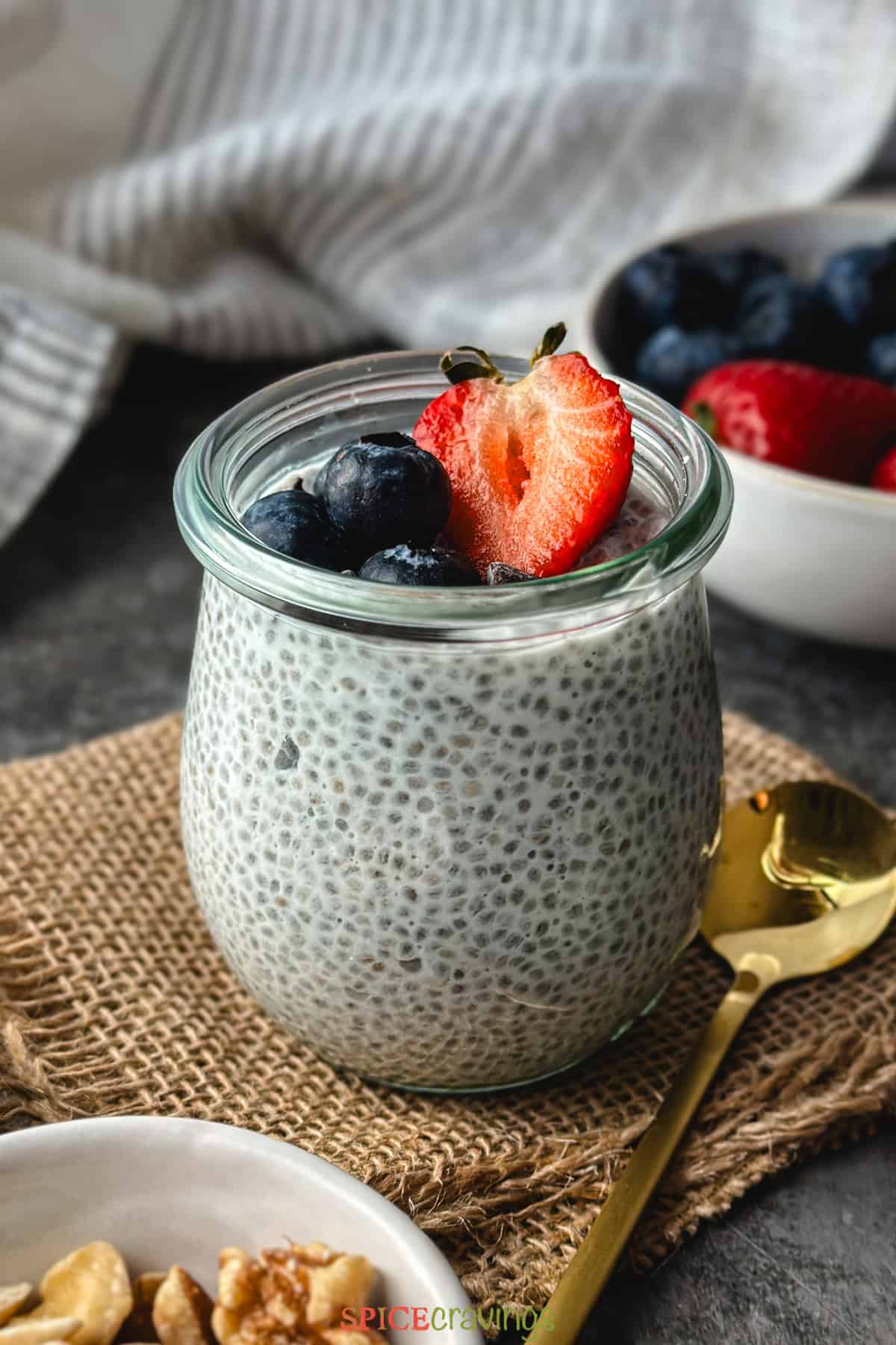 coconut chia pudding in glass jar topped with halved strawberry and blueberries
